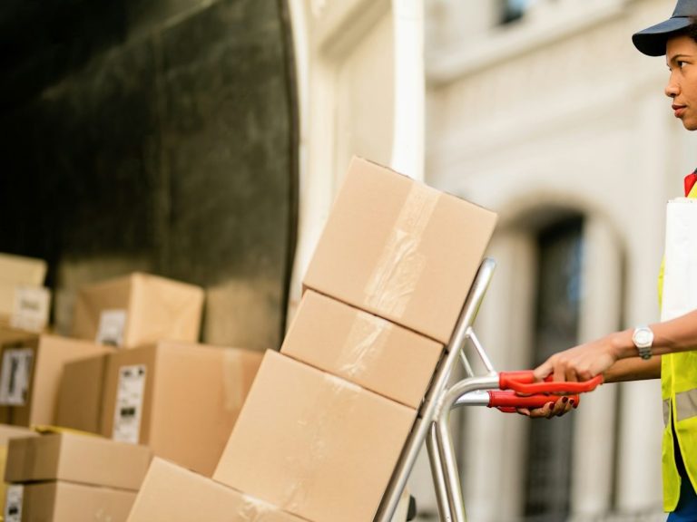 Person using a hand trolley to move stacked cardboard boxes.