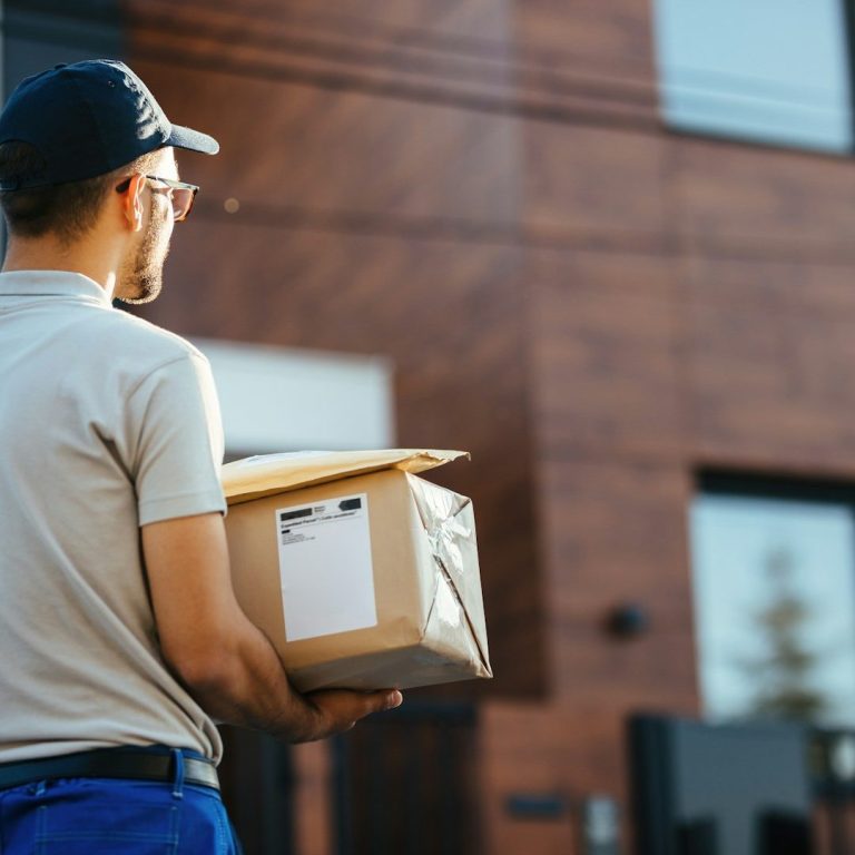 Delivery person holding a package outside a modern building.